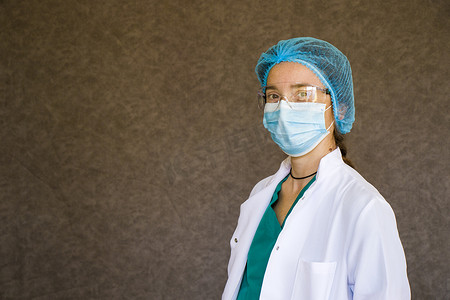 护士戴口罩摄影照片_女医生肖像，戴面具、眼镜、手套和制服的医生。