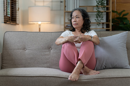 沮丧的年长亚裔妇女独自坐在家里。
