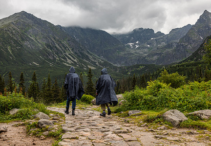 蒙面舞会男女摄影照片_两名身穿派克大衣的蒙面徒步者在塔特拉山雨中行走