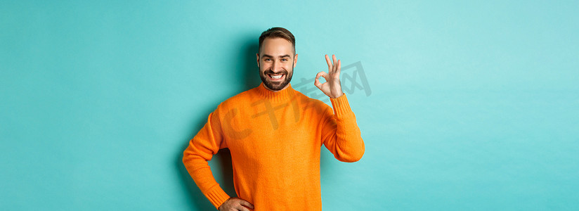 自信帅哥的形象，表现出好的手势、赞同和同意，就像一些好东西，站在橙色毛衣上