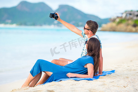 蜜月假期摄影照片_蜜月假期在白色沙滩上拍照的幸福情侣