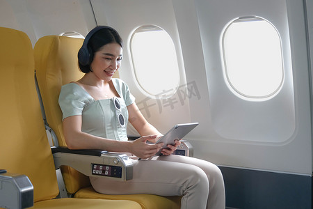 年轻女性在头等舱飞行期间使用移动播放列表和配件收听最喜欢的歌曲，女性在飞机板上娱乐时通过智能手机享受耳机中的音乐