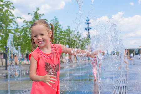 阳光明媚的炎热日子里，可爱的小女孩在街头喷泉里玩得开心