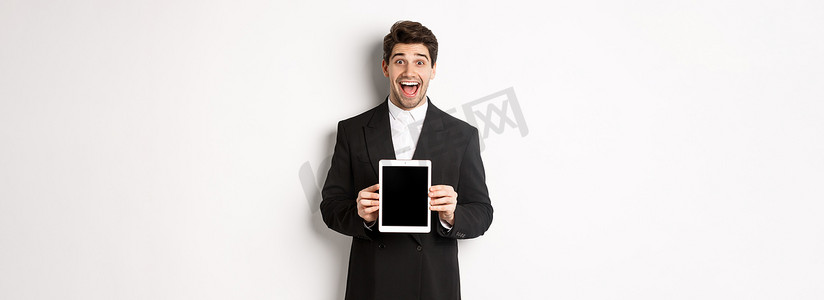 穿着时髦西装的迷人男性企业家形象，展示数字平板电脑屏幕，微笑着惊讶地站在白色背景上