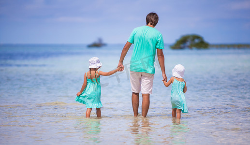 年轻父亲和他的两个小孩在海边散步的背影