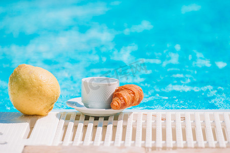 美味的早餐柠檬、咖啡、泳池边的羊角面包
