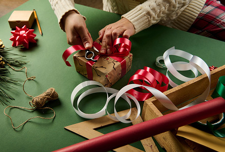 特写女人包装圣诞礼品盒，用闪亮的红色装饰丝带系起来。