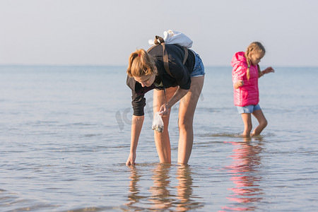沙滩捡贝壳摄影照片_带着孩子走在沙滩上捡贝壳的女人