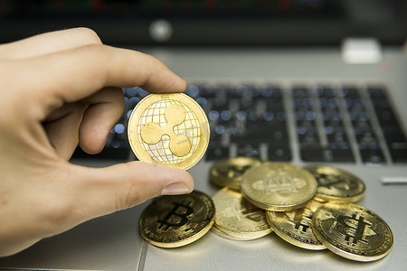 拿着金币的手摄影照片_男性商人手拿着 Ripple 硬币在笔记本电脑键盘和一堆金币的背景上。