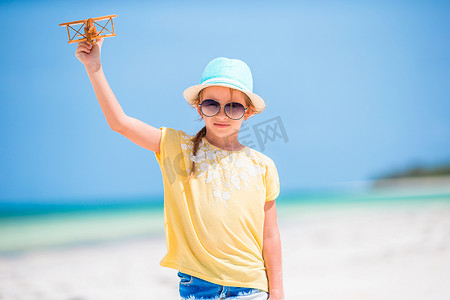 玩具行动摄影照片_白色沙滩上手拿玩具飞机的快乐小女孩