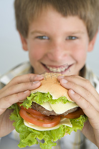 男孩吃汉堡摄影照片_微笑着吃芝士汉堡的小男孩