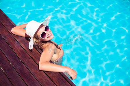 戴着墨镜和草帽的美女靠在泳池边的木甲板上
