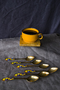 勺子黄色摄影照片_桌上的复古勺子、银器、黑咖啡杯