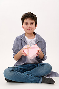 帅气的微笑男孩，带着可爱的情人节、母亲节或妇女节礼物，装在心形粉色礼盒里