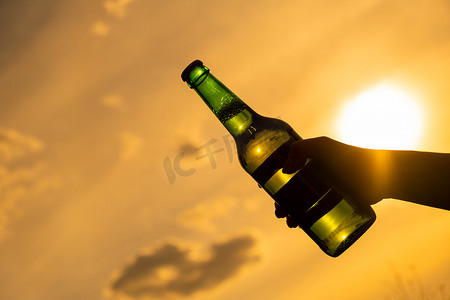 女人拿着一瓶啤酒在户外反对天空背景。
