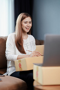 独立的年轻亚洲女性在线卖家的小企业主正在使用计算机并接受订单来包装产品以交付给客户。