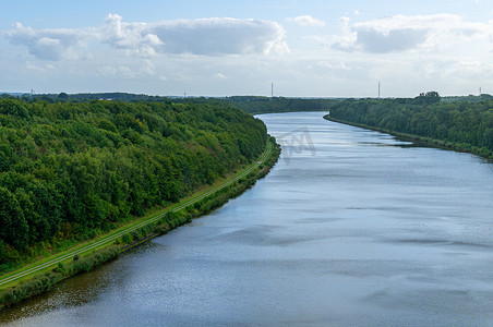 河岸摄影照片_一条在北方云层下的绿色河岸之间流淌的河流