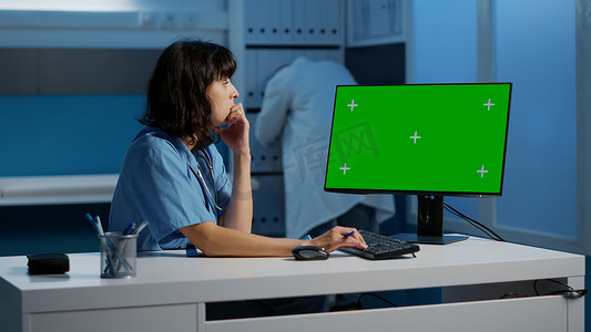 站在办公桌前的护士看着带绿屏模板的电脑