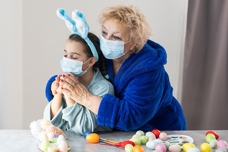 戴着医用口罩的祖母和孙女正在为假期画复活节彩蛋。