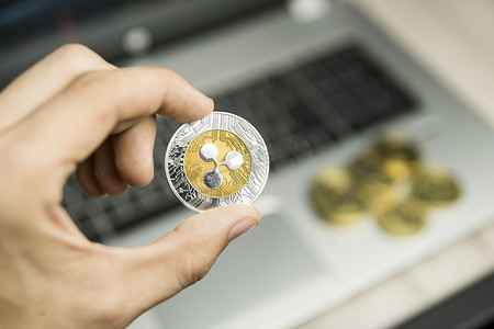 拿着金币的手摄影照片_男性商人手拿着 Ripple 硬币在笔记本电脑键盘和一堆金币的背景上。