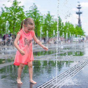 阳光明媚的炎热日子里，可爱的小女孩在街头喷泉里玩得开心