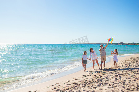 风筝玩具摄影照片_快乐的年轻家庭，有两个孩子，在沙滩上放风筝