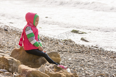 快乐的女孩坐在海边的一块岩石上，望着远方