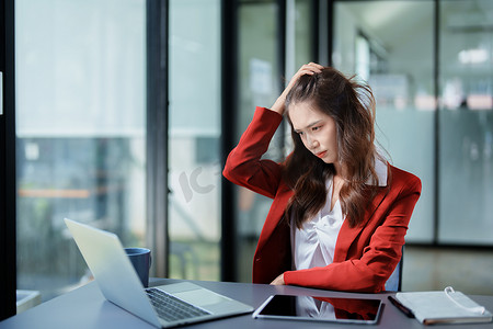 一位亚洲年轻女性的画像，她在清晨使用办公桌上的手机、财务文件和笔记本电脑时表情严肃