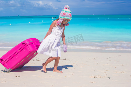 戴手套冬天摄影照片_戴着冬日帽子和手套的可爱女孩带着行李在沙滩上散步