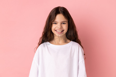 满意的穿 T 恤的小女孩带着露齿的微笑看着镜头，表达积极的表情
