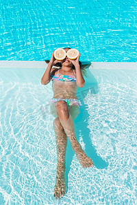 小女孩柠檬摄影照片_在背景游泳池的眼睛附近用柠檬半遮住眼睛的小女孩