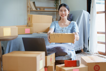 开始使用电脑笔记本电脑微笑的独立亚洲女性的小企业企业家在线营销包装盒项目和 SME 交付概念的欢快成功