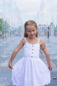 在阳光明媚的炎热日子里，快乐小女孩的肖像在街边喷泉里玩得开心