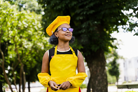 穿着厨师帽和黄色围裙制服的黑人非洲儿童厨师女孩在户外微笑。
