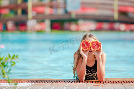 背景游泳池上，小女孩用橙色的一半遮住眼睛，靠近眼睛