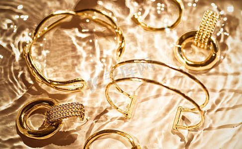 金手镯、耳环、戒指、金水背景上的珠宝