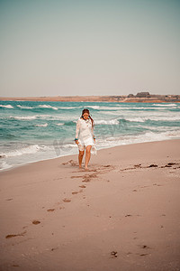 在沙滩上穿着白色长裙和银首饰的波西米亚风格模特。