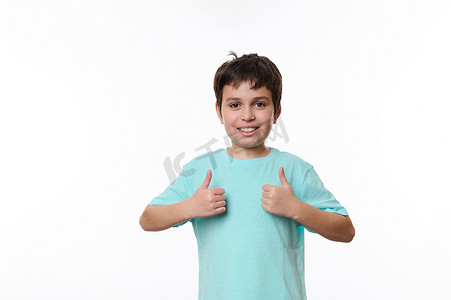 穿着蓝色休闲 T 恤的愉快少年的肖像，在文本的复制空间显示大拇指，白色背景