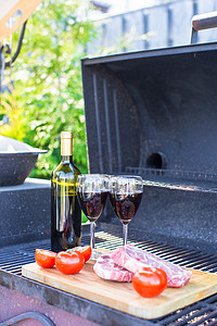 户外烧烤架摄影照片_户外烧烤时的一瓶红酒、牛排和西红柿
