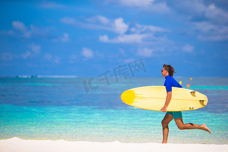 沙滩冲浪摄影照片_快乐的年轻冲浪人拿着冲浪板在沙滩上奔跑