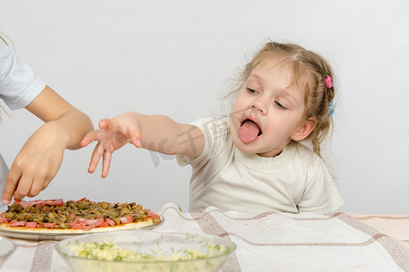 伸出手摄影照片_小女孩用舌头伸出手拉比萨饼，这是为她姐姐准备的