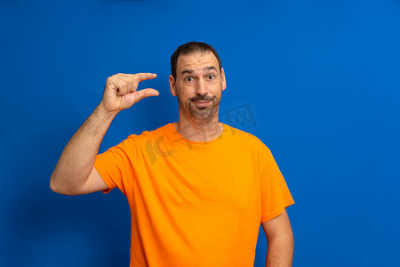 西班牙裔男子站在蓝色背景上，脸上带着怀疑的表情，用手做着小手势，用手指看着和相机。