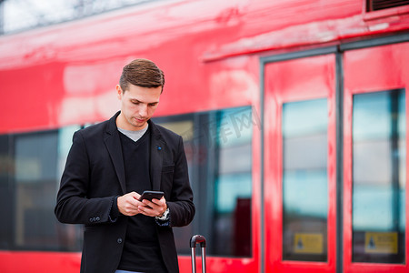 年轻的白人男子带着智能手机和行李在车站乘火车旅行