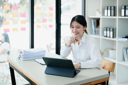 一位深思熟虑的亚洲女商人的肖像，她正在使用办公桌上的电脑查看财务报表并制定营销计划