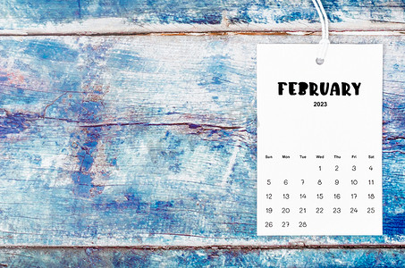 2023蓝色背景摄影照片_2023 年 2 月的日历页用白色绳子挂在旧的蓝色木背景上。