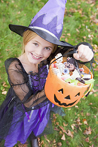万圣节穿着女巫服装在户外拿着糖果的小女孩