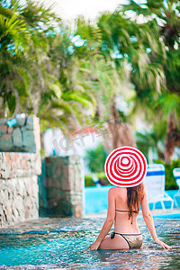 戴着大红帽的年轻美女在安静的游泳池享受暑假