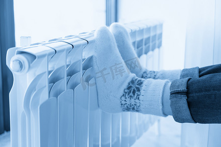 穿着羊毛袜、脚放在加热器上取暖的女人