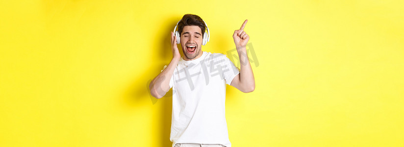 快乐的男人戴着耳机听音乐，指着黑色星期五的促销优惠，站在黄色背景上