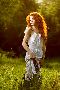 森林光芒摄影照片_走在日落森林光芒下的红头发人女孩